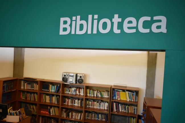 Cartel verde con letras blancas "biblioteca", de fondo una estantería llena de libros